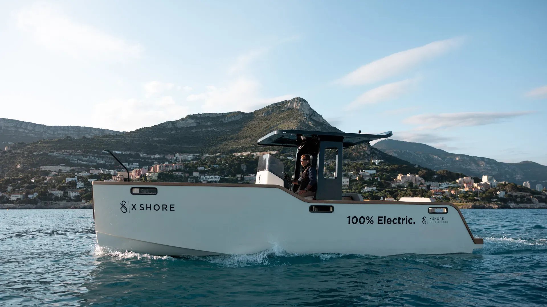 Side profile of the X Shore Eelex 8000 cruising along a mountainous coastline