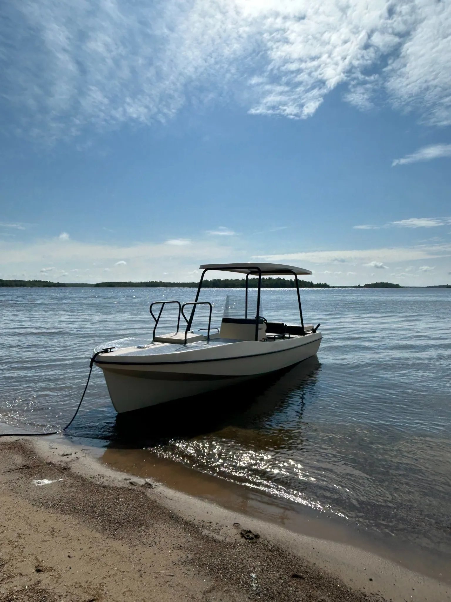 Elvene Amber solar-electric boat moored at the shoreline under a bright summer sky.