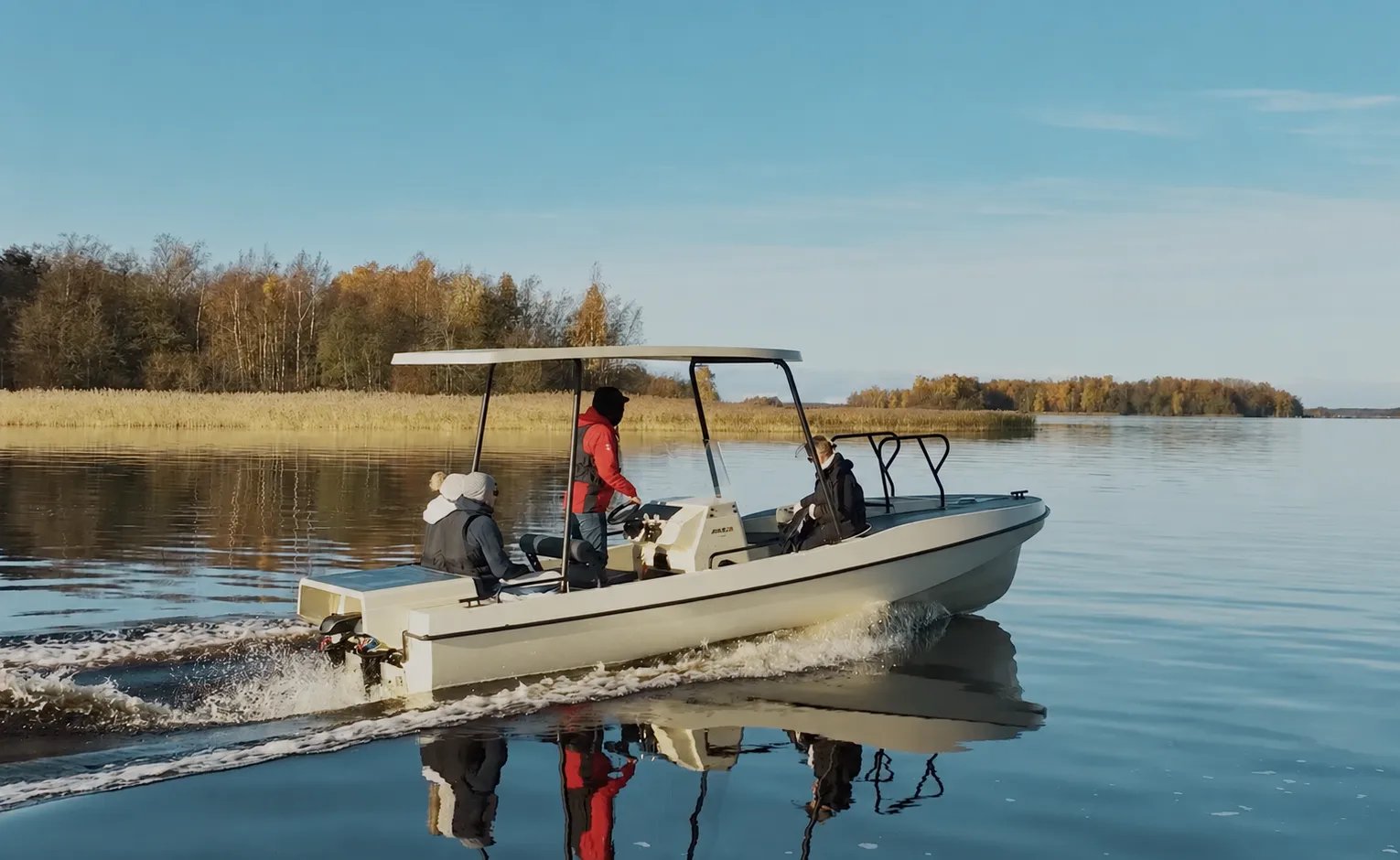 Side view of the Elvene Amber solar-electric boat underway on a calm lake with three passengers on board.