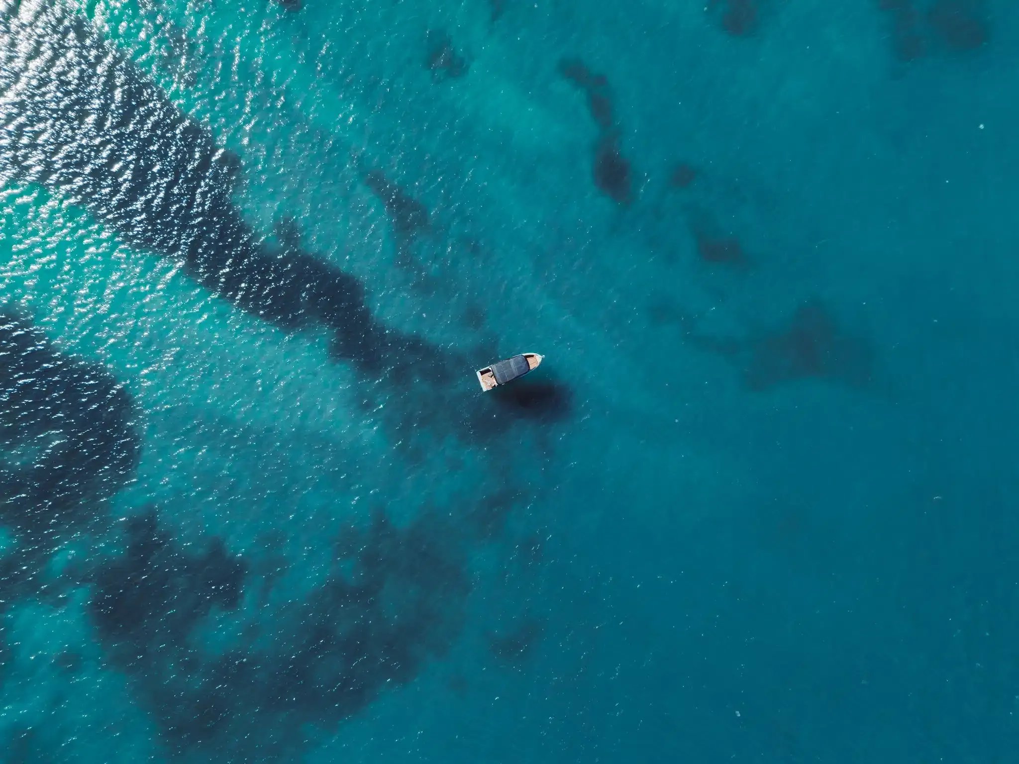 Top-down aerial view of the Helios Omega electric boat on clear turquoise water.