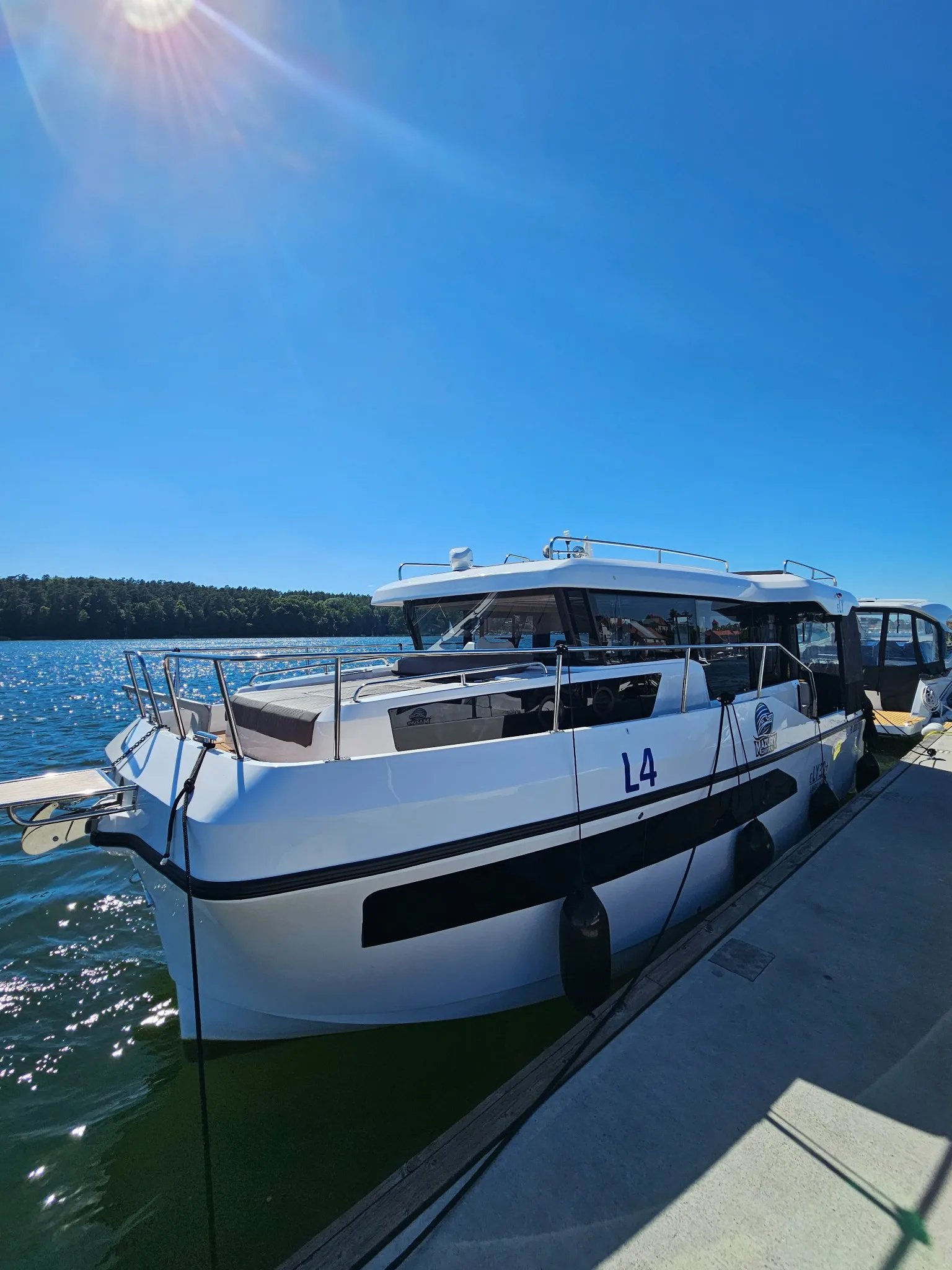 Front three-quarter view of the Lamdo eLY30+ electric houseboat moored beside a dock.