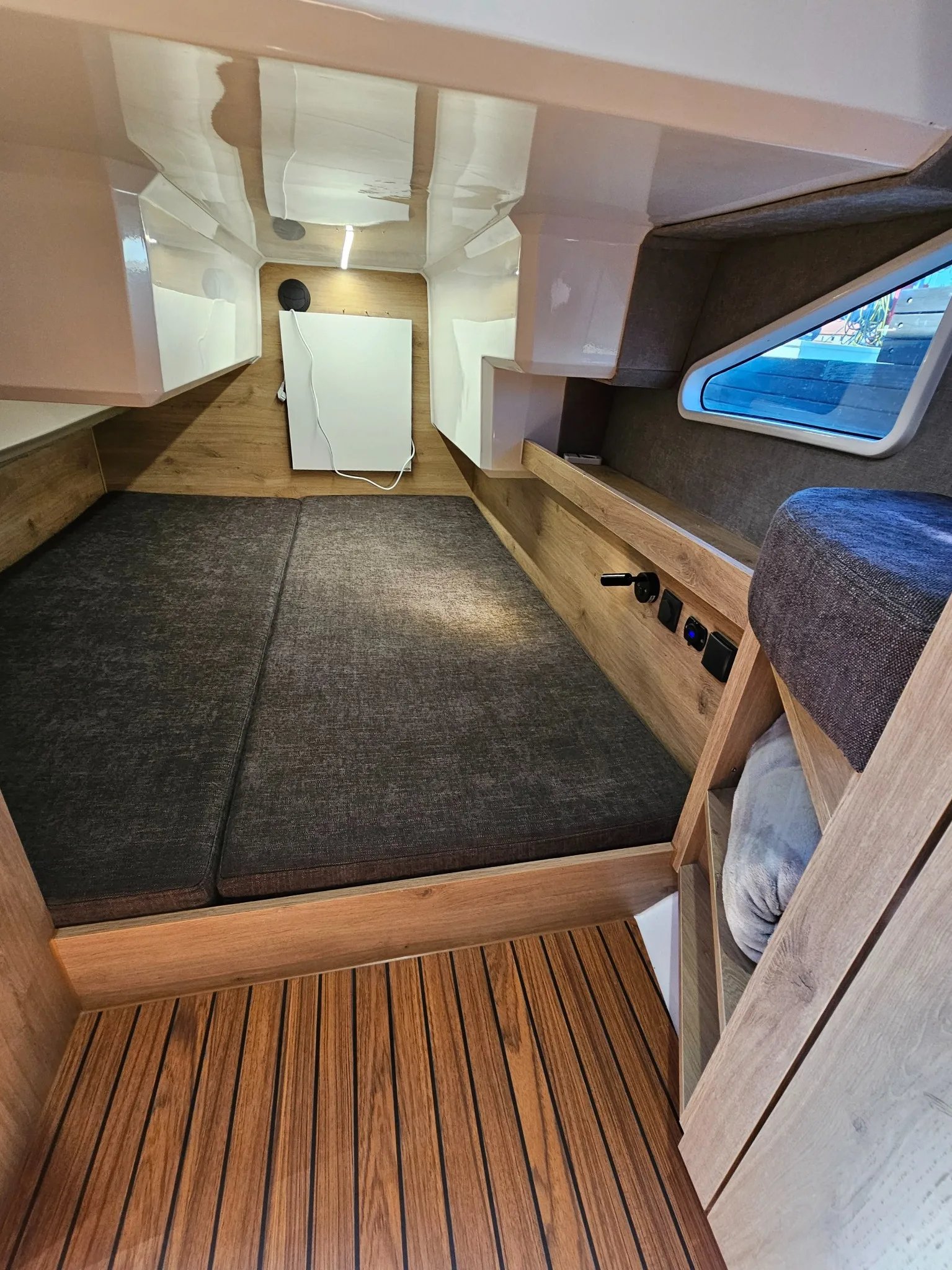 Forward cabin of the Lamdo eLY30+ with a double berth, side window and wood-finish storage.