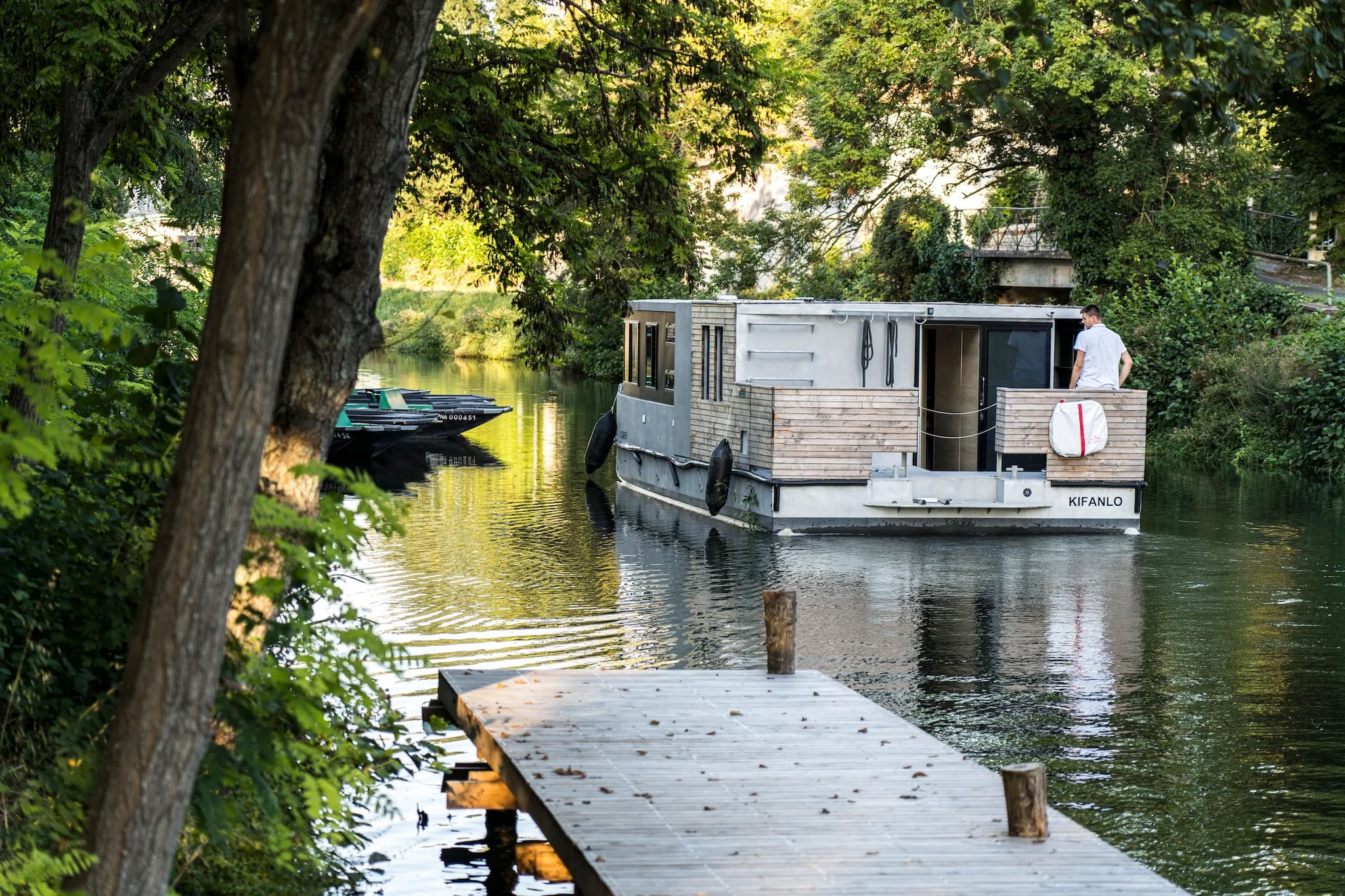 Zenriver electric houseboat by BAB Boat approaching a wooden pontoon near traditional flat-bottomed marsh boats