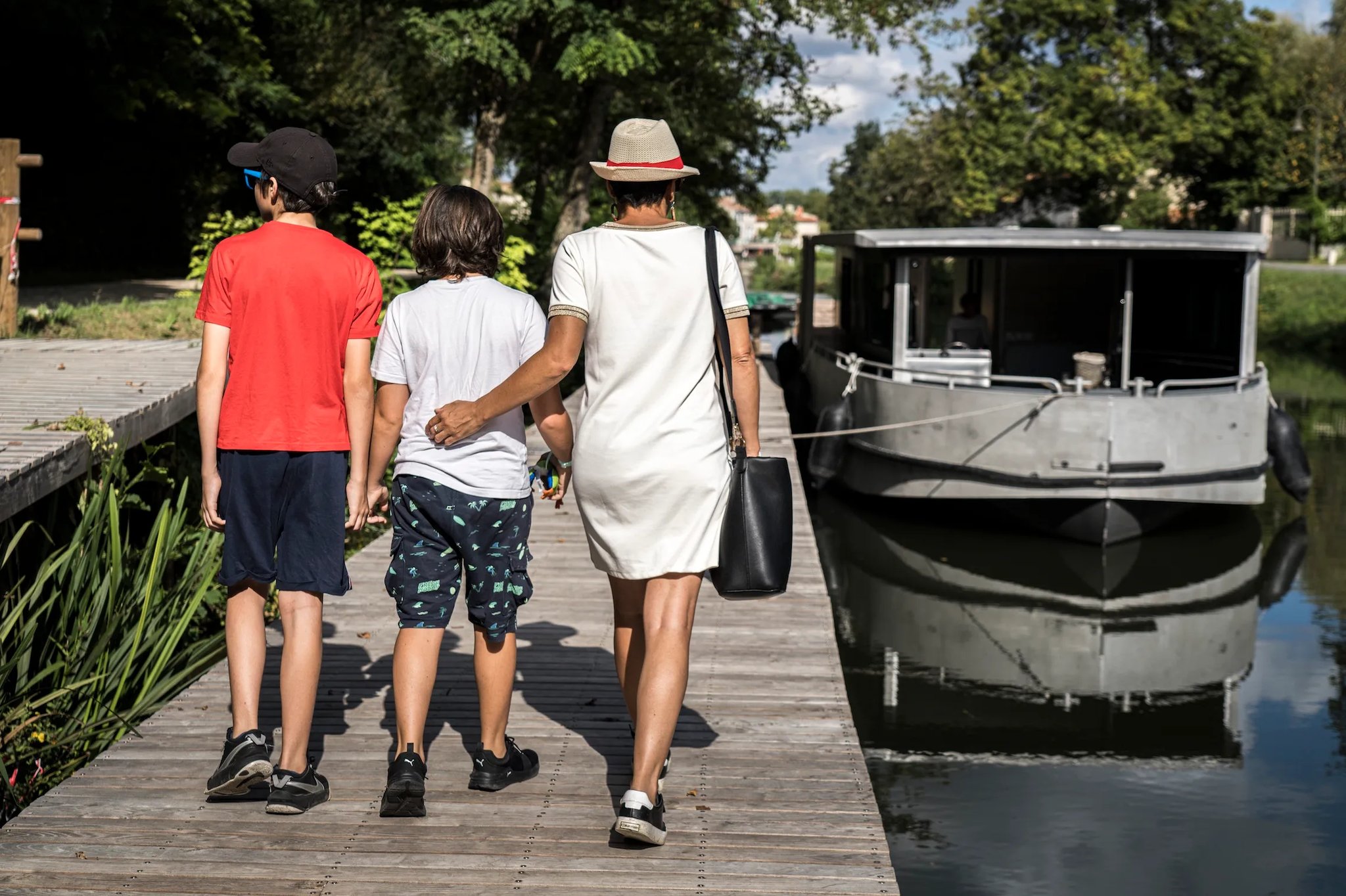 Family walking along a pontoon to board an electric houseboat for a Marais Poitevin river tour