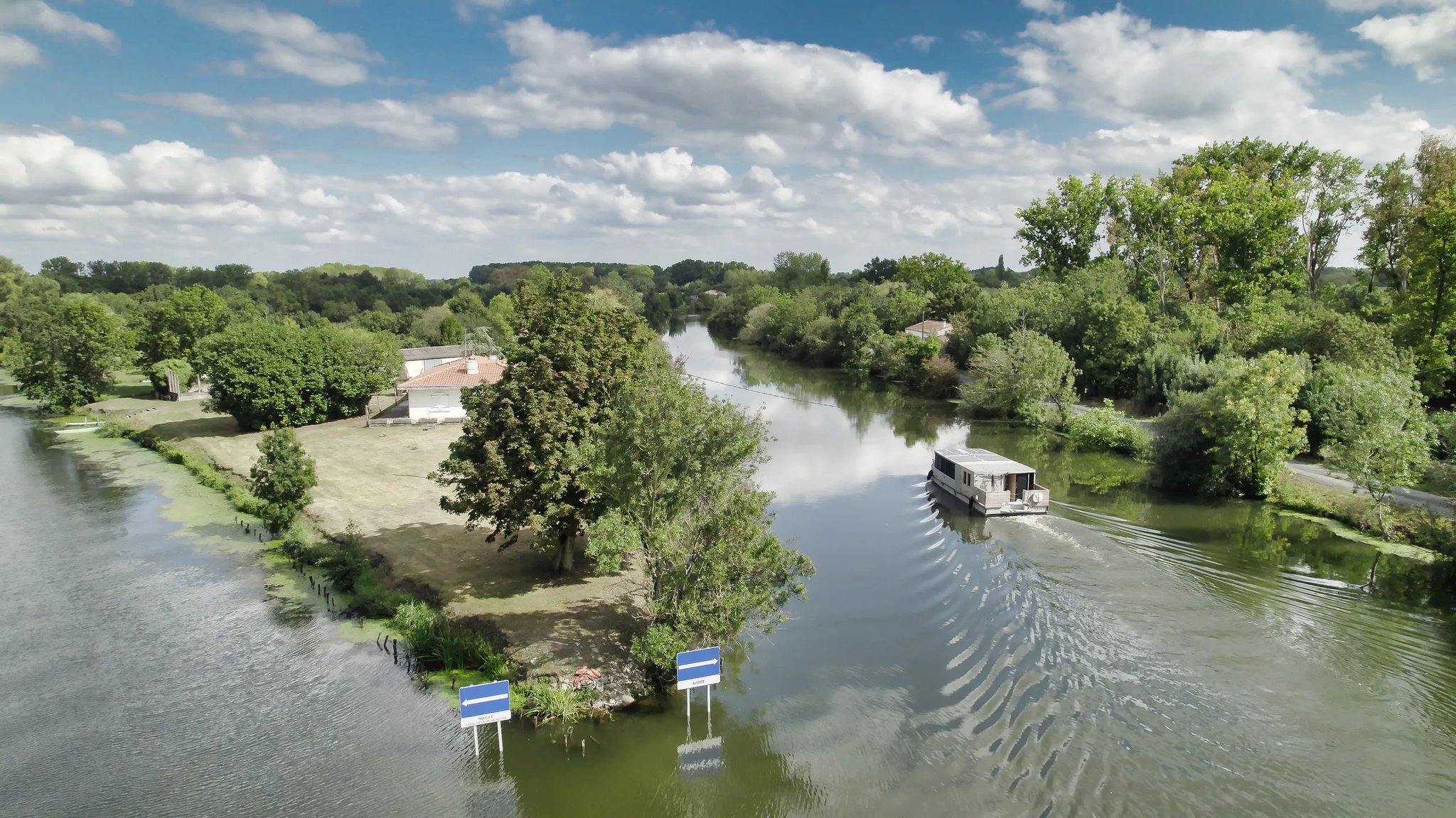 Aerial view of the Zenriver electric houseboat cruising a wide canal through the Marais Poitevin wetlands