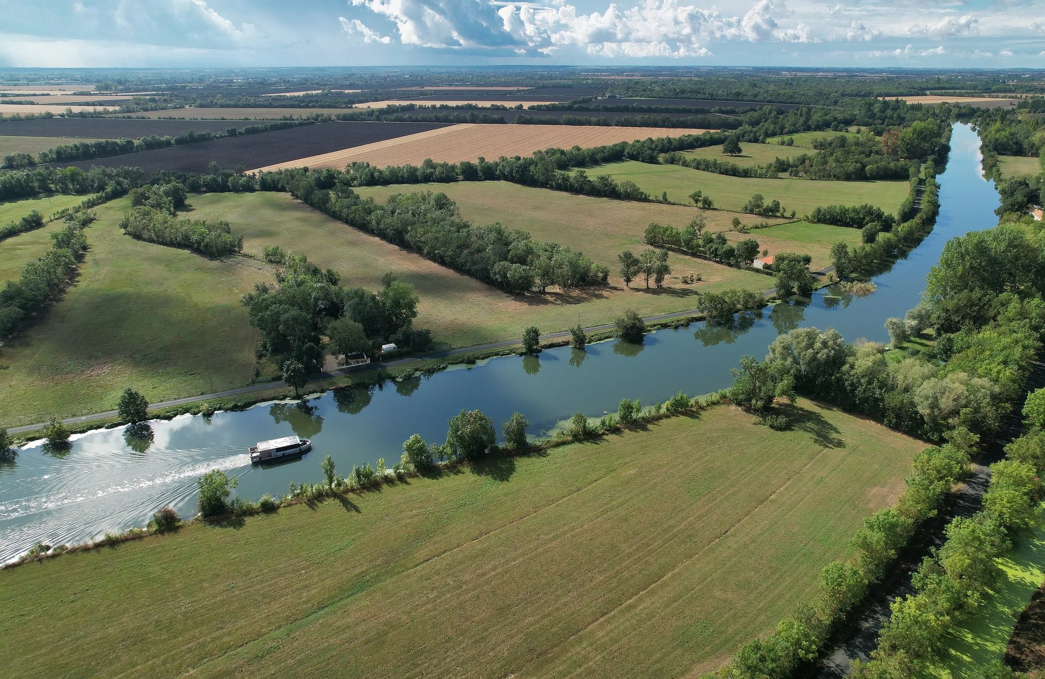 Aerial view of the Zenriver electric houseboat cruising a straight canal through Marais Poitevin farmland