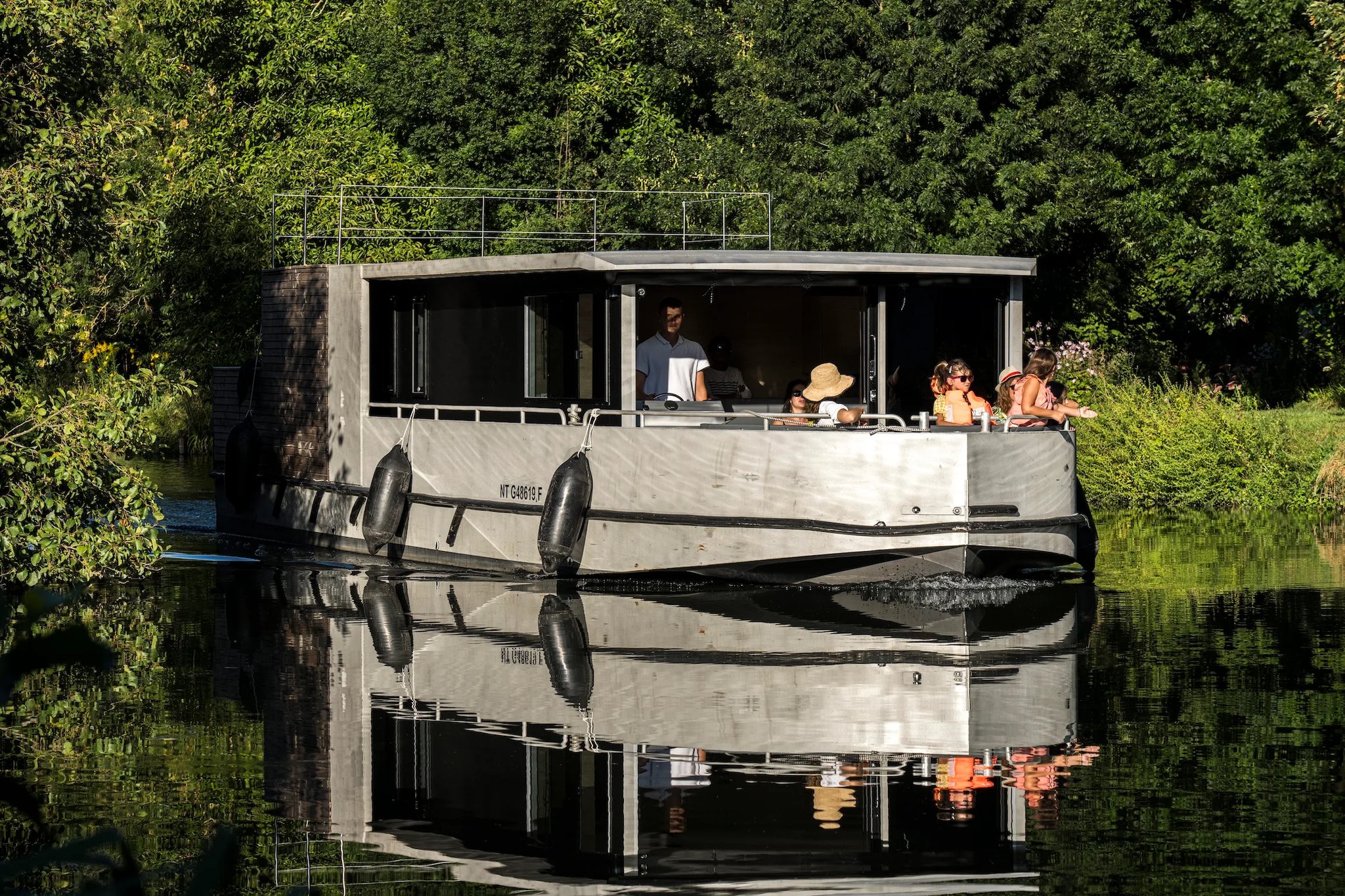 Family cruising a tree-lined canal aboard the Zenriver electric houseboat in the Marais Poitevin