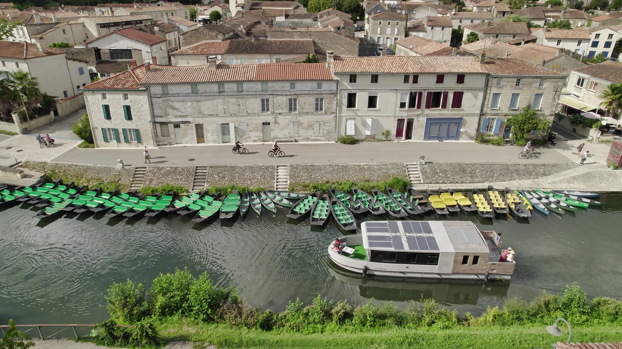 Solar-powered Zenriver electric houseboat cruising past a historic village quay lined with traditional green boats